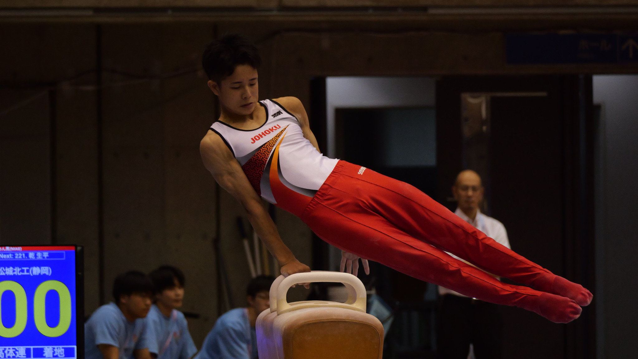 白と赤のユニフォームを着た選手が男子あん馬で演技する場面